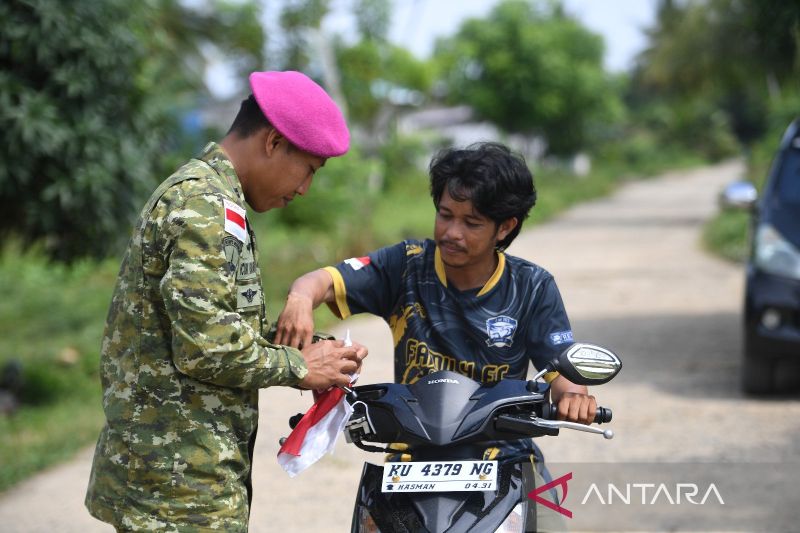 Prajurit Korps Marinir TNI AL yang tergabung dalam Satuan Tugas Marinir Pulau Terluar (Satgas Mar Pam Puter) XXX memasang Bendera Merah Putih di sepeda motor milik warga di Tanjung Aru, Sebatik Timur, Kabupaten Nunukan, Kalimantan Utara. Sumber foto: Antara