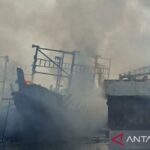 Petugas memadamkan kapal terbakar saat sandar di Dermaga Muara Angke, Jakarta Utara, Minggu (19/7/2026). Sumber foto: Antara